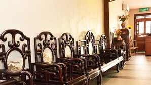 A row of wooden chairs with ornate carvings, a tiled floor, and a reception desk with a vase of flowers. - Cheng Ho Residence (Malacca City)