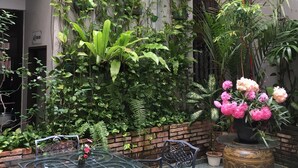 A patio area with a glass table and metal chairs, surrounded by lush greenery and potted plants. - Cheng Ho Residence (Malacca City)