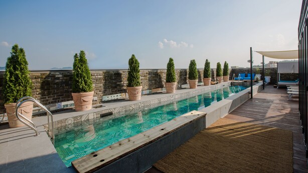A rooftop pool with a clear view of the city skyline, surrounded by potted plants and a wooden deck. - Hotel Museo (Cheongju)