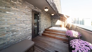 A rooftop terrace with a brick wall, wooden deck, a hot tub, and potted flowers. - Hotel Museo (Cheongju)