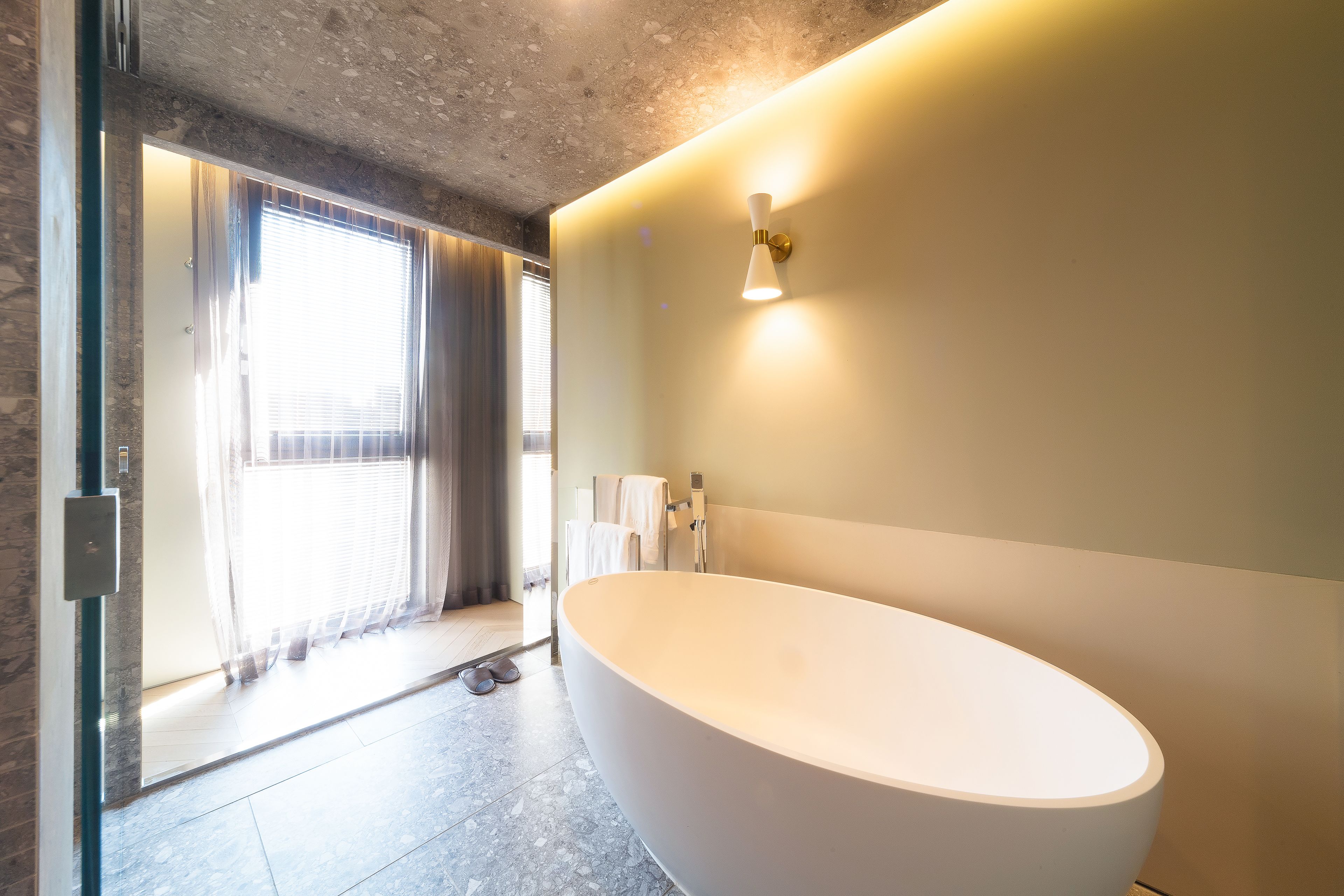 A modern bathroom with a freestanding bathtub, a shower area, and a large window allowing natural light.