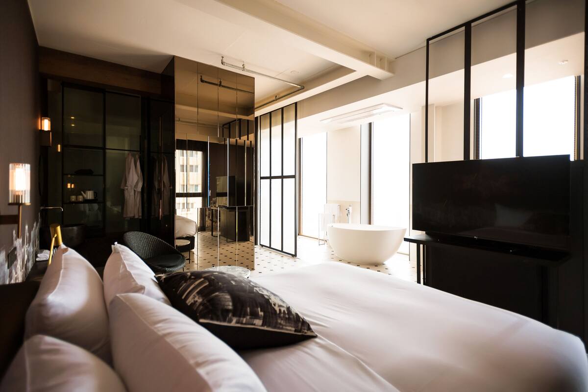 A modern hotel room with a large bed, a flat-screen TV, a bathtub, and a walk-in closet.