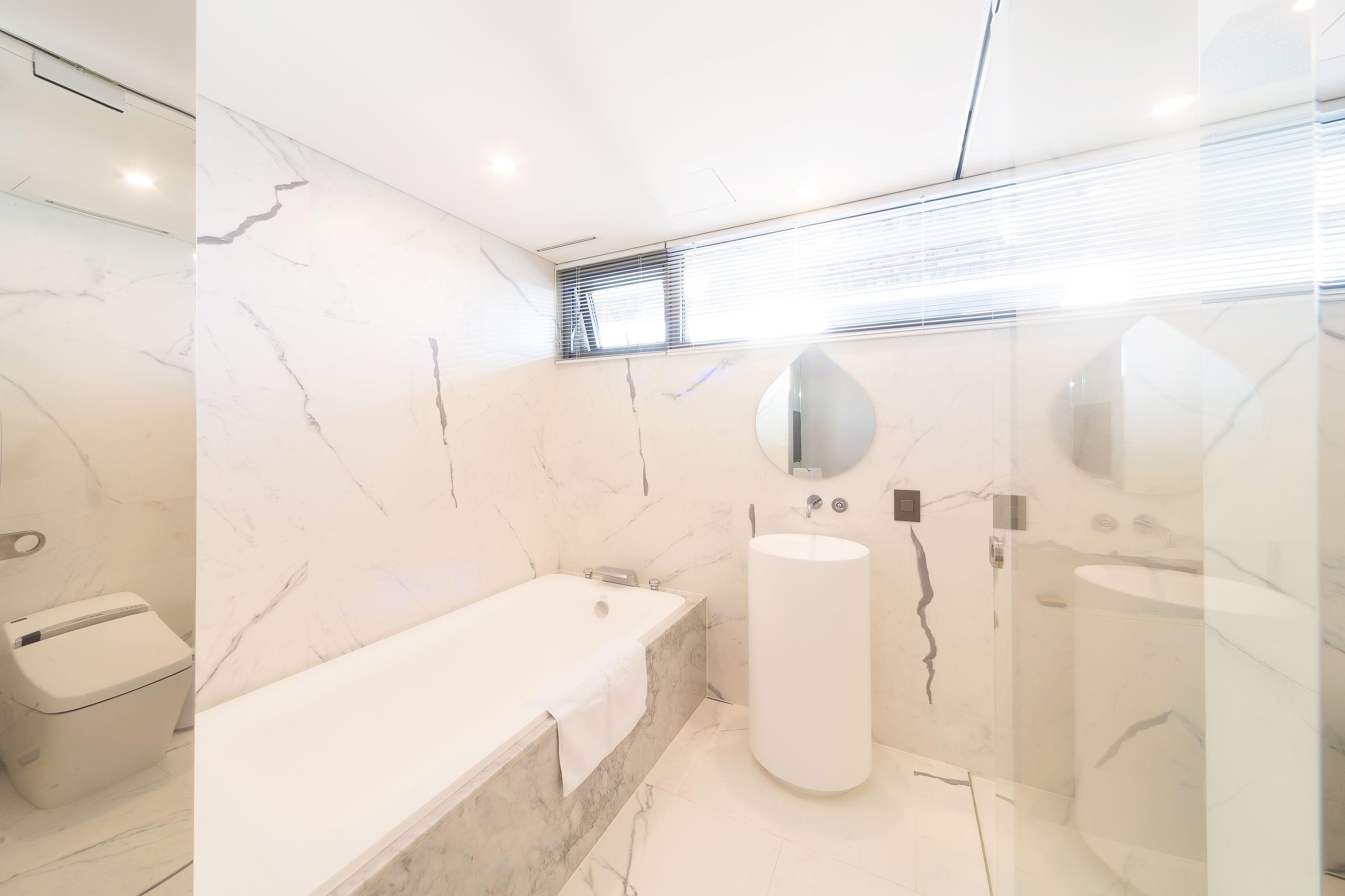 A modern bathroom with a marble vanity, a bathtub, and a large sink.