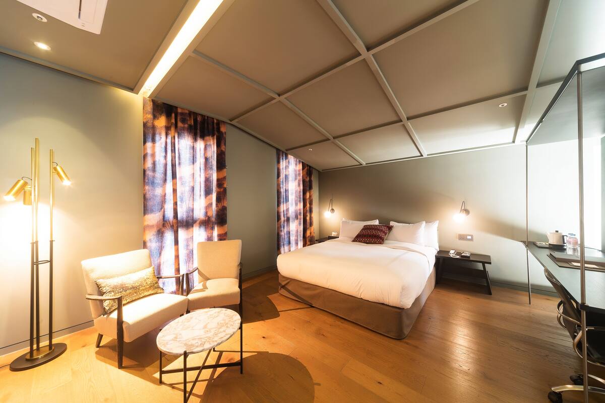 A modern bedroom with a large bed, a chair, a small table, and a desk with a chair.