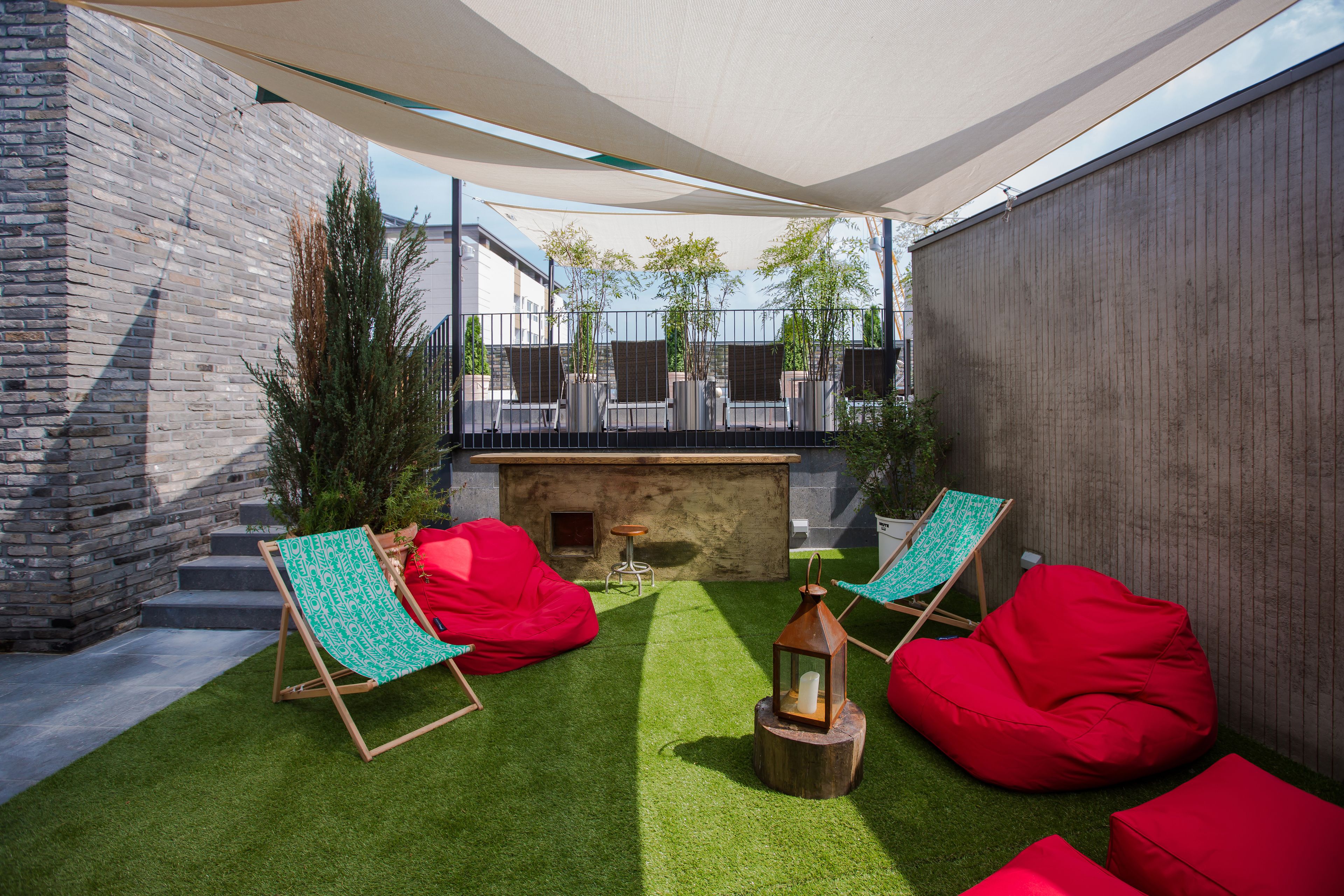 An outdoor patio with artificial grass, red bean bags, and two green and white striped lounge chairs.