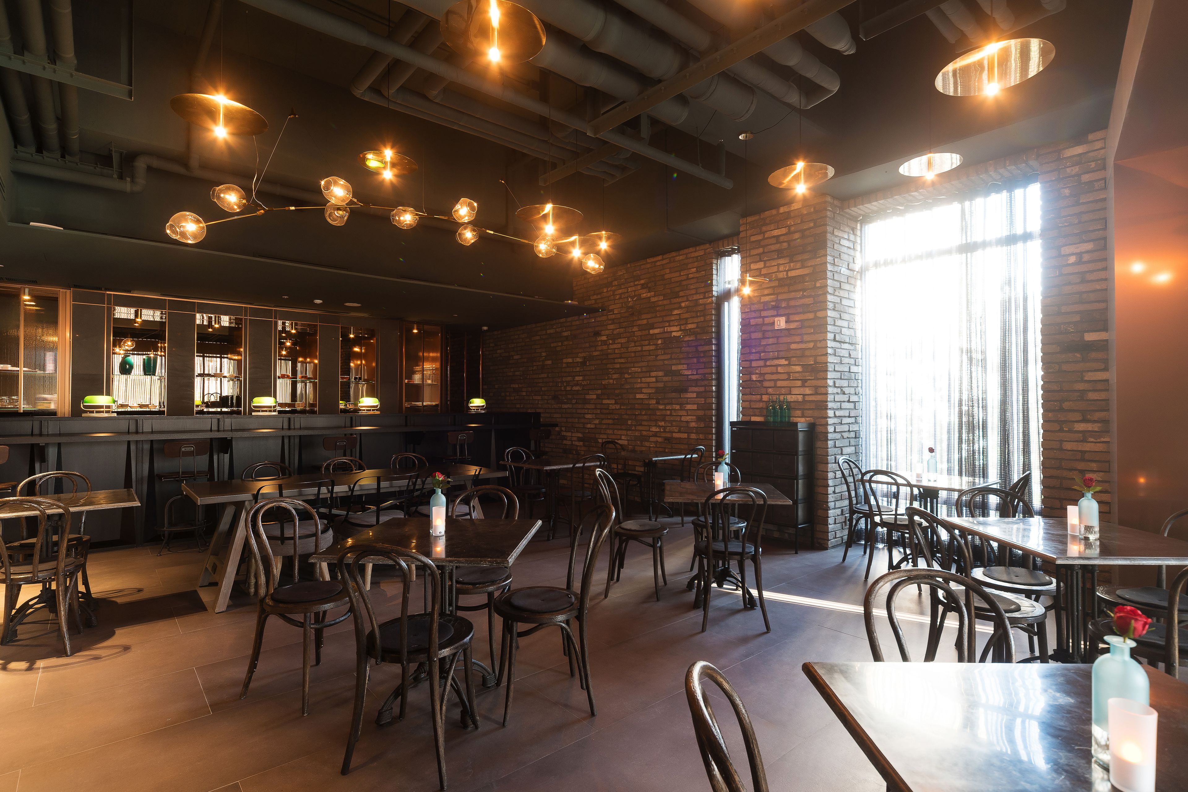 Interior de restaurante con paredes de ladrillo, techos a la vista y lámparas colgantes. Mesas y sillas dispuestas para comer.