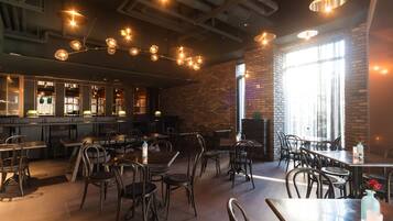 Interior de restaurante con paredes de ladrillo, techos a la vista y lámparas colgantes. Mesas y sillas dispuestas para comer.