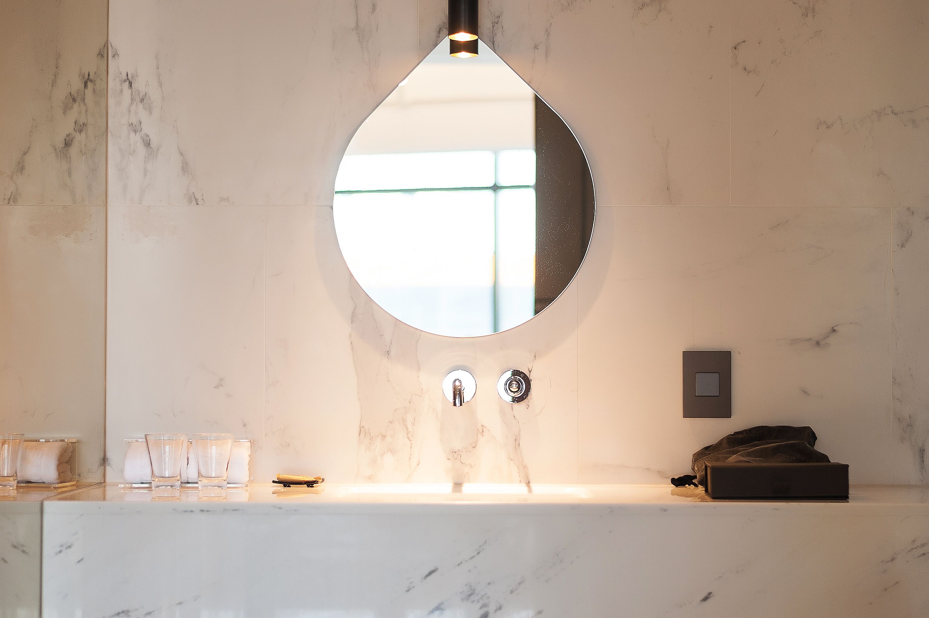 A bathroom with a marble sink, a round mirror, and a towel rack.