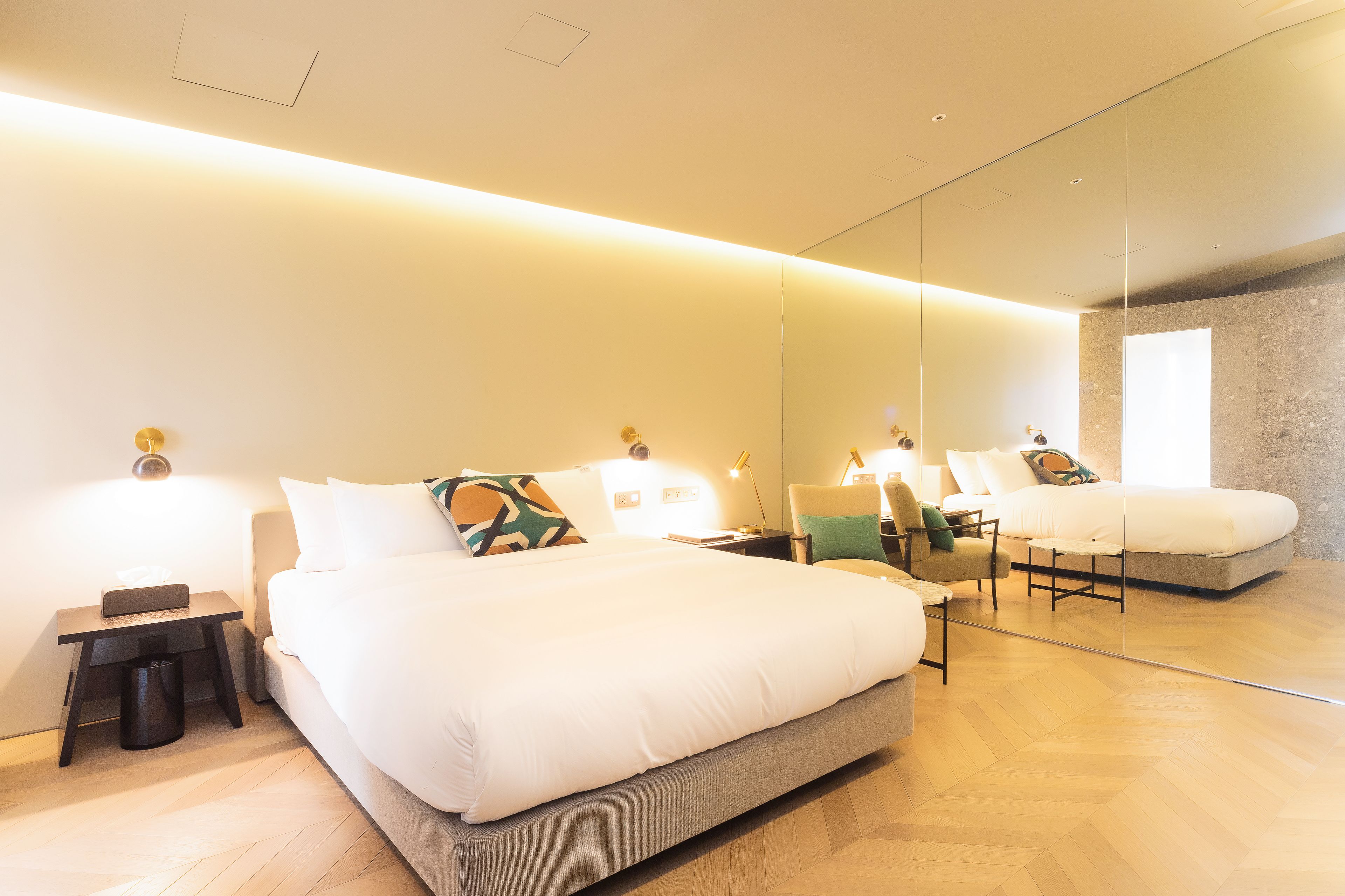 A modern hotel room with a large bed, bedside tables, a chair, and a mirror.