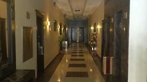 Pasillo de hotel con piso de diseño ajedrezado, puertas a ambos lados e iluminación en la pared.