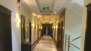 Un pasillo de hotel con piso de baldosas brillantes, paredes con lámparas y una escalera a la derecha.