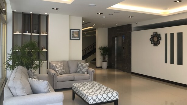 Eine moderne Lobby mit einer Couch, Hocker, Topfpflanzen, einer Treppe und einer Wanduhr.