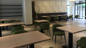 Ein moderner Essbereich mit mehreren Tischen und grünen Stühlen, der ein aufgeräumtes, minimalistisches Design mit einer Kombination aus natürlichem und künstlichem Licht aufweist.