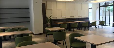 Un comedor moderno con varias mesas y sillas verdes, que presenta un diseño limpio y minimalista con una combinación de iluminación natural y artificial.