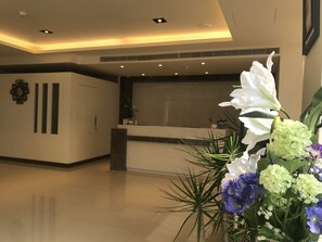 A reception area with a modern design, featuring a reception desk, a clock, and a potted plant with flowers. - ML Hotel (Chiayi City)