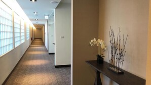 A hallway with a patterned carpet, a dark wooden table with a potted plant, and a wall-mounted decorative piece.