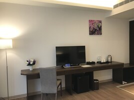 Habitación de hotel moderna con televisión de pantalla plana, escritorio con silla, un pequeño bote de basura y cafetera.