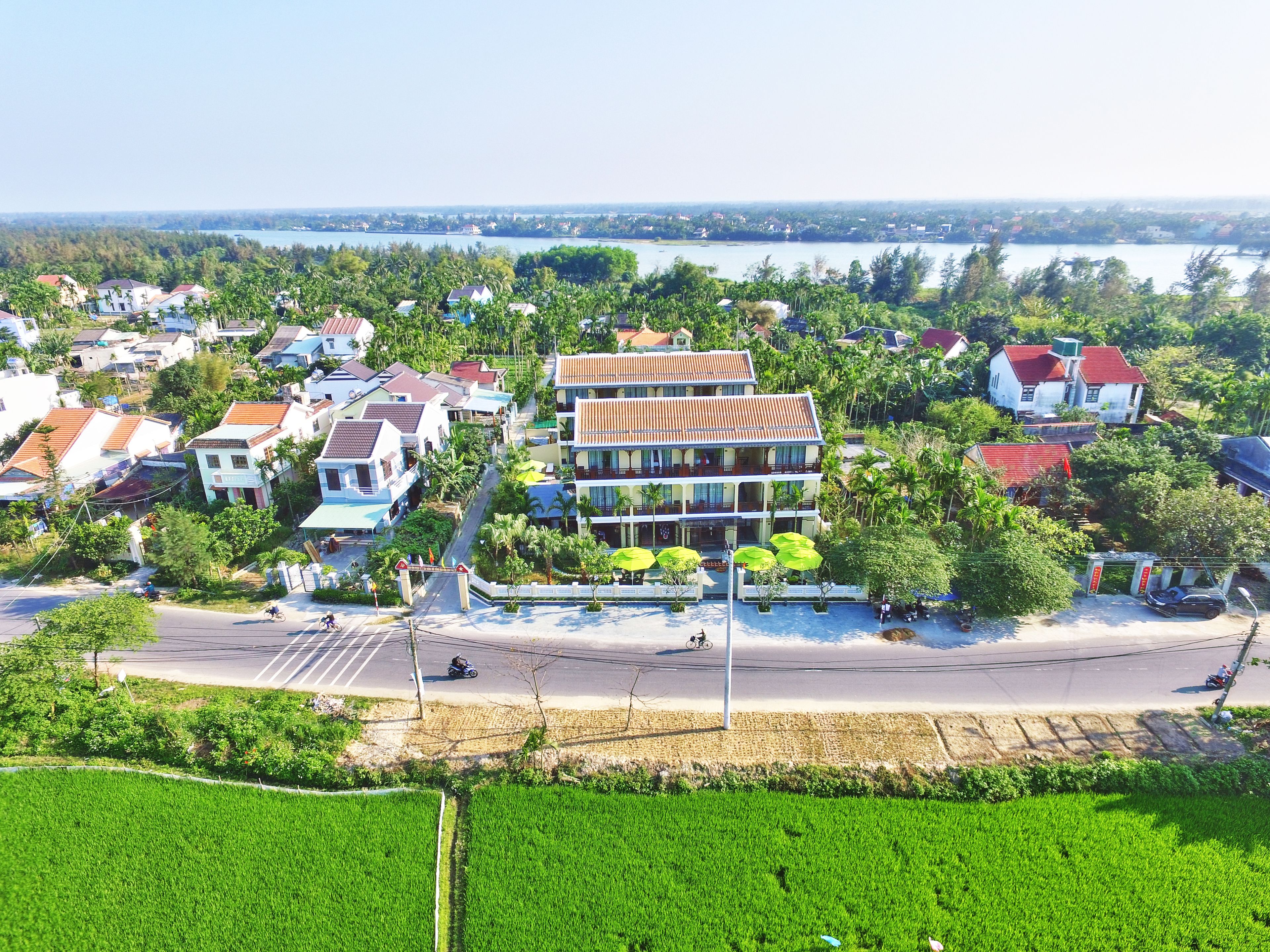 Vista aérea de un pueblo costero con edificios residenciales, un edificio central de dos pisos con balcones y una carretera que lleva al mar.