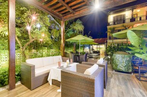 Área de estar externa com móveis de vime, uma mesa coberta e um guarda-sol verde.