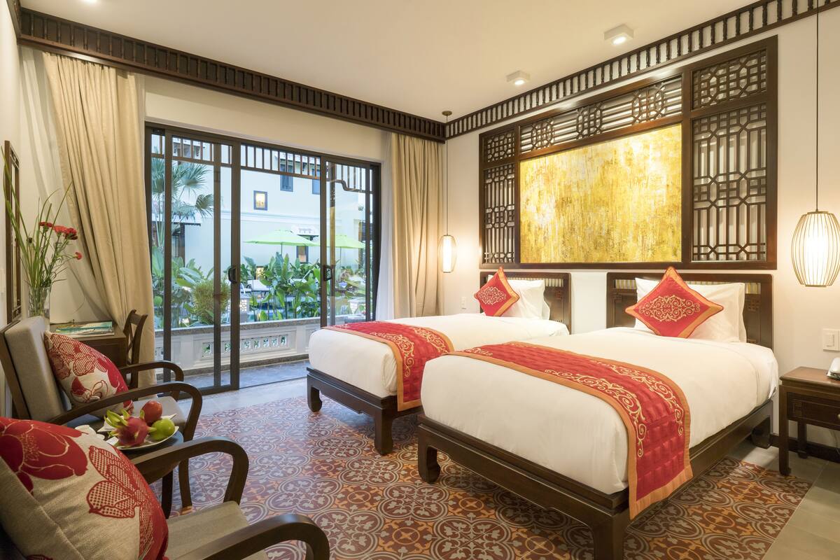 A hotel room with two beds, a large window, a decorative wall panel, and a view of the outdoors.