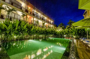 Vista noturna de um hotel com piscina, rodeado por vegetação exuberante e palmeiras.