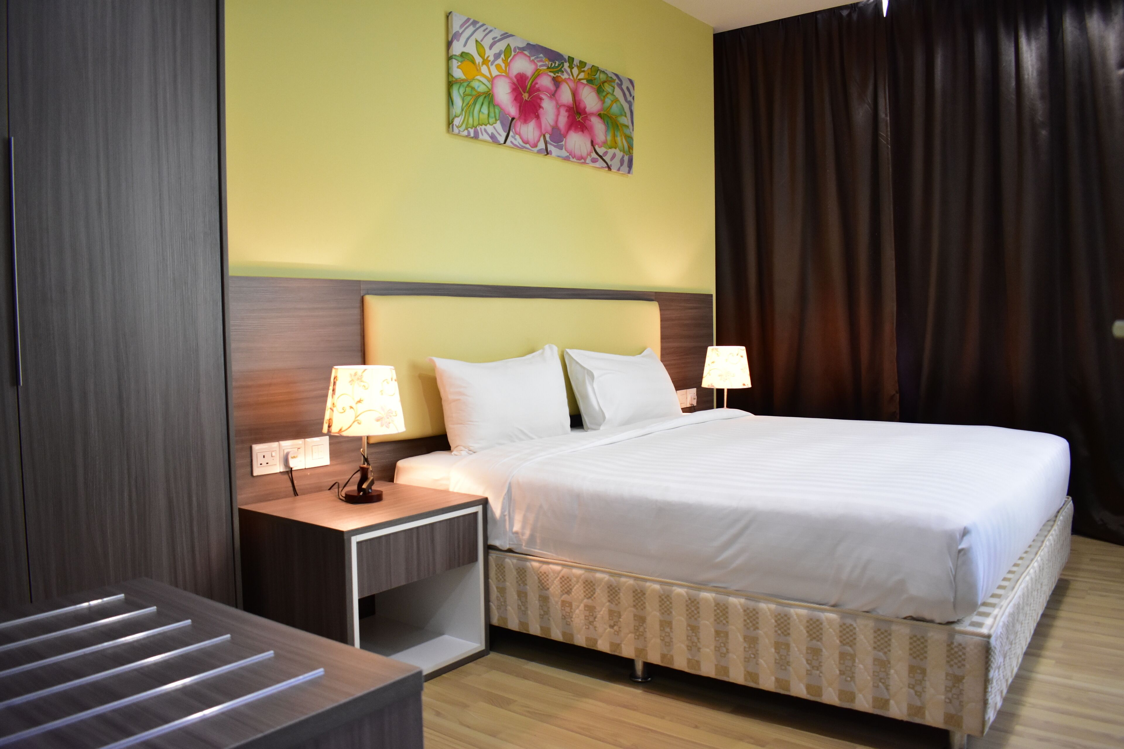 A hotel room with a bed, nightstands, a lamp, a painting on the wall, and a curtain.