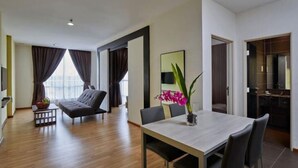 En moderne stue med sofa, spisebord og stole. Der er et stort vindue med gardiner, et fladskærms-tv og en vase med blomster.