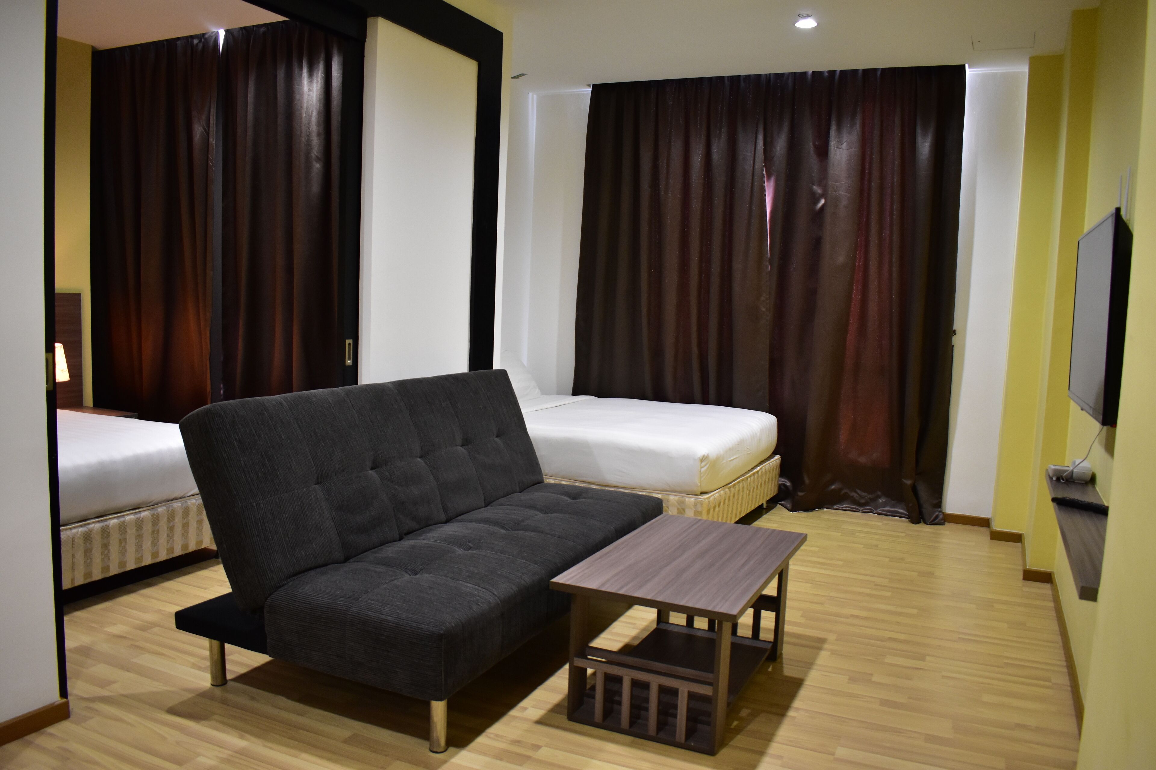 A modern hotel room with a sofa, a small table, a bed, and a TV.