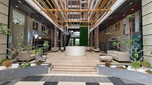 A modern lobby with a central seating area, a staircase, and a green wall.