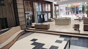 En rummelig lobby med et ternet gulv, moderne siddepladser og udsigt til en bygning med skiltet "ASSAM HOUSE".