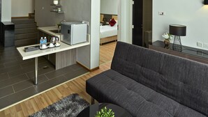 En rummelig opholdsstue med sofa, sofabord og et tekøkken med køleskab og vask.
