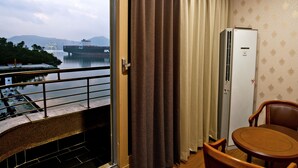 Habitación de hotel con balcón y vista a un cuerpo de agua, un refrigerador y una mesa de comedor con sillas.