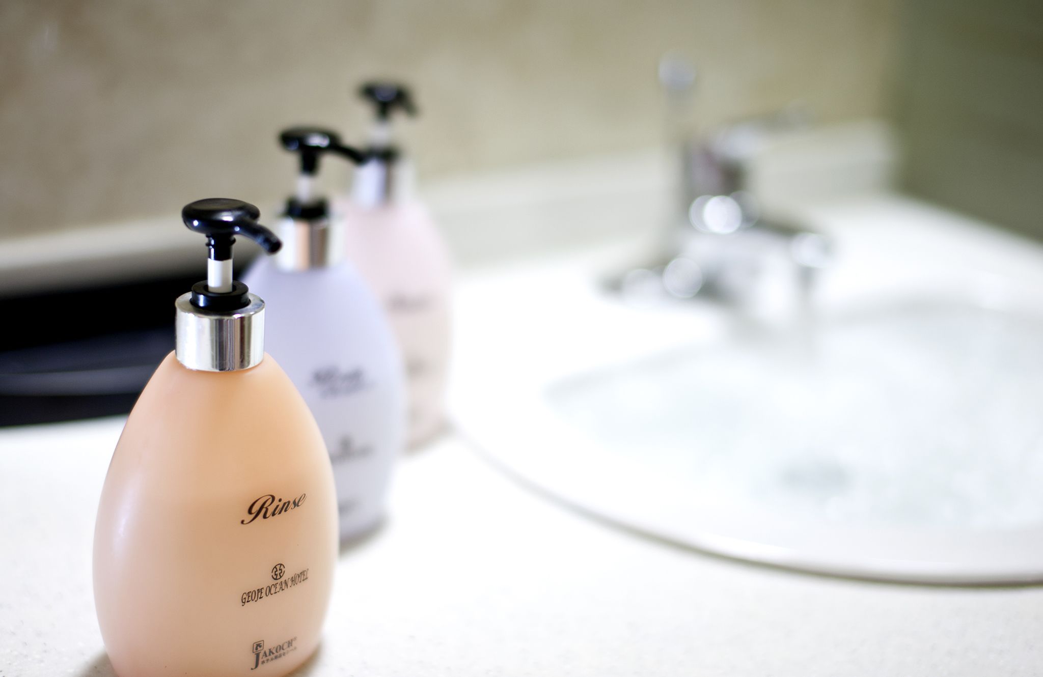 A bathroom with a sink and three soap dispensers labeled "Rinse" and "GEOJE OCEAN HOTEL".