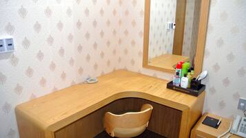 Habitación de hotel con un escritorio de madera, una silla, un espejo, un teléfono y artículos de tocador sobre el escritorio.