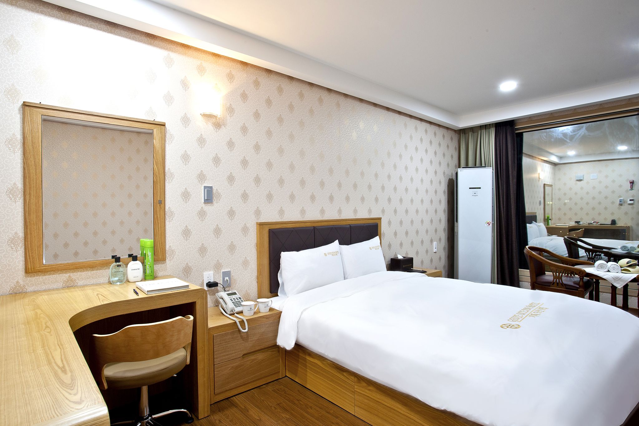 Habitación de hotel con una cama grande, un escritorio con silla, un espejo y una pequeña cocina.
