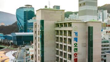 A multi-story hotel with a prominent sign, a parking area, and a modern building in the background.