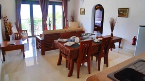 Un coin repas avec une table dressée pour quatre personnes, des chaises en bois, un canapé et une vue sur l’extérieur grâce à de grandes fenêtres.