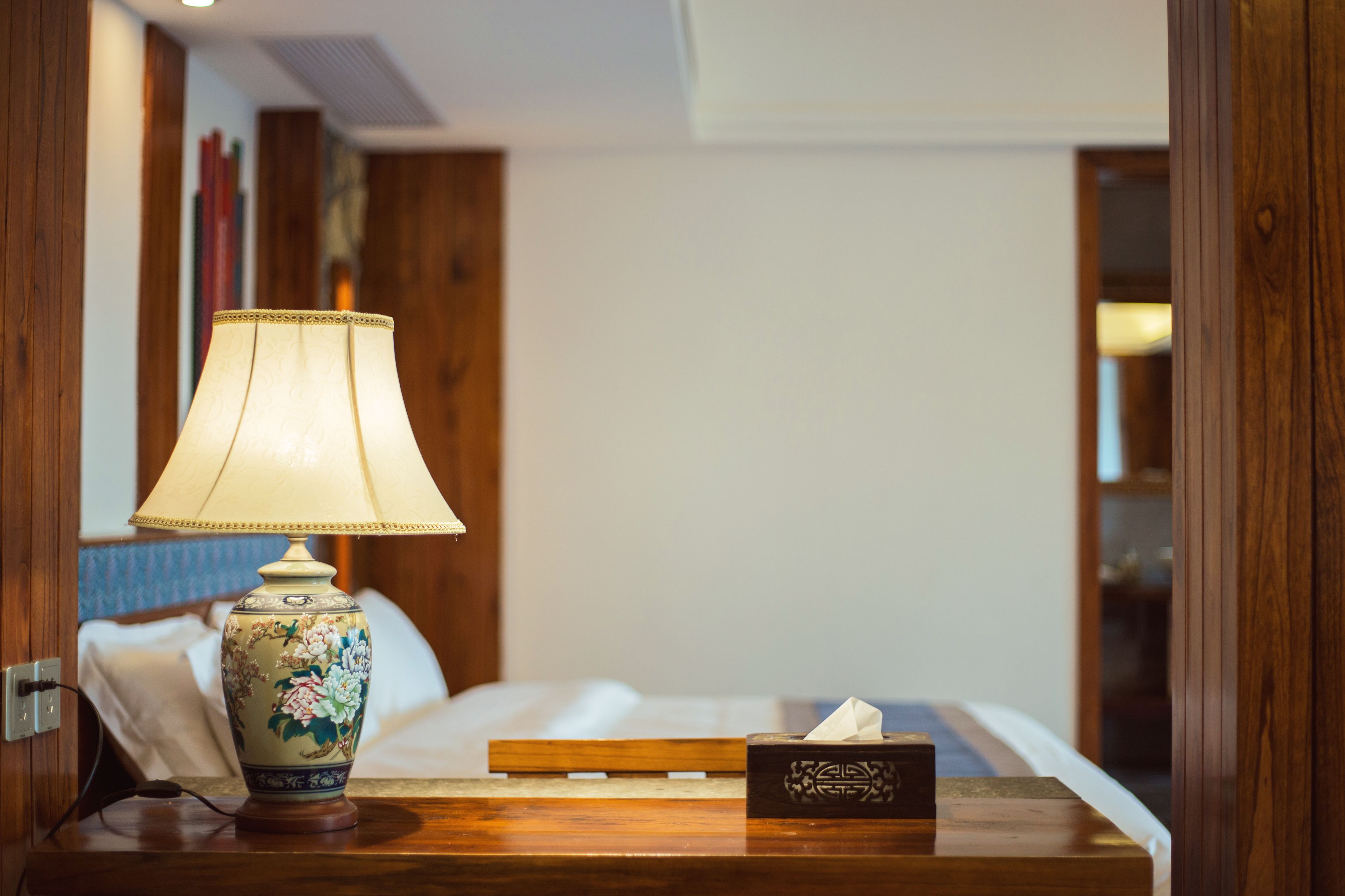 A neatly made bed with a bedside table featuring a lamp and a tissue box.