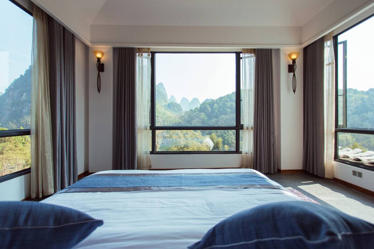 A bedroom with a large bed, a view of a mountainous landscape, and two wall-mounted light fixtures.