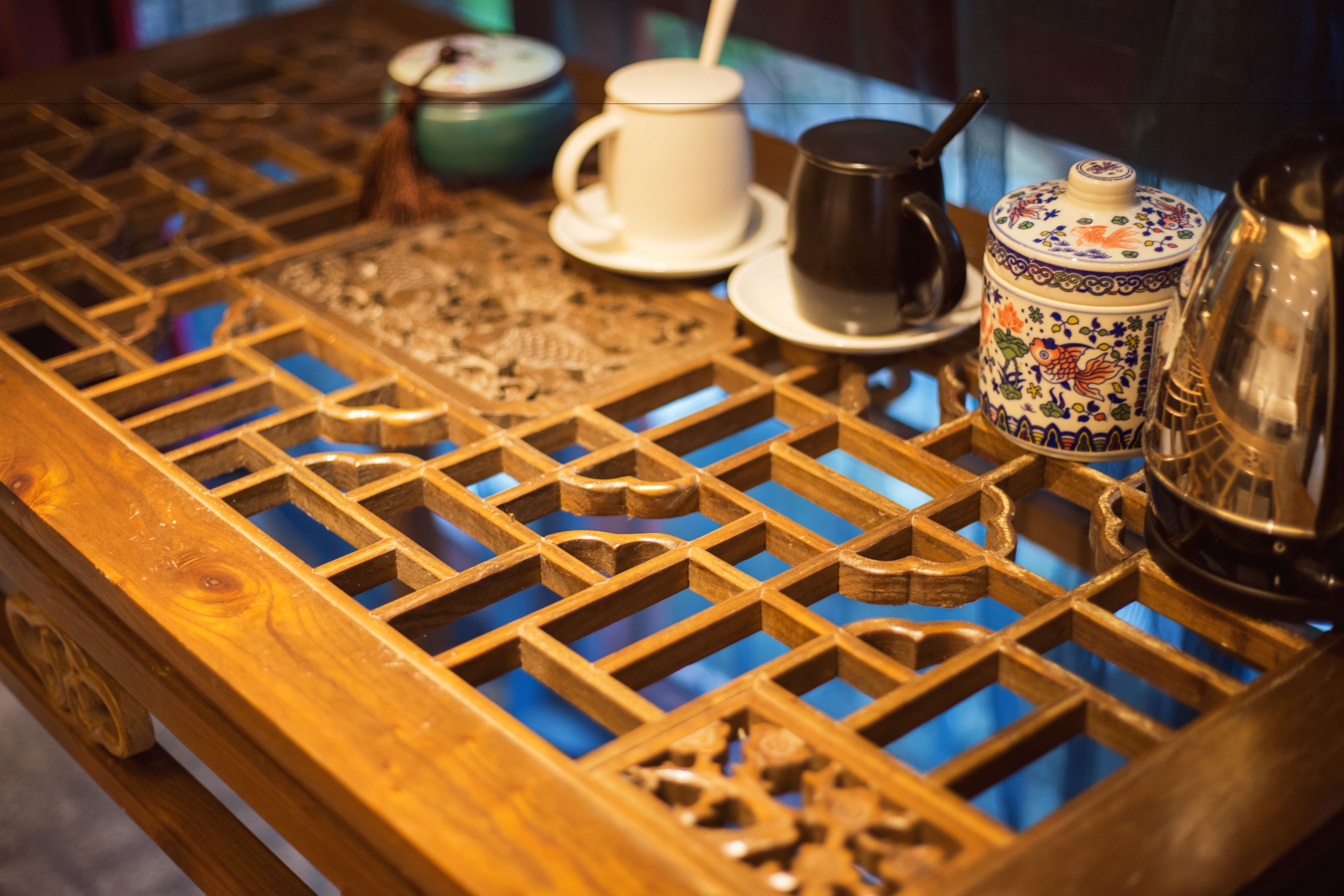 A wooden table with intricate carvings and a tea set including a teapot, cups, and a saucer.
