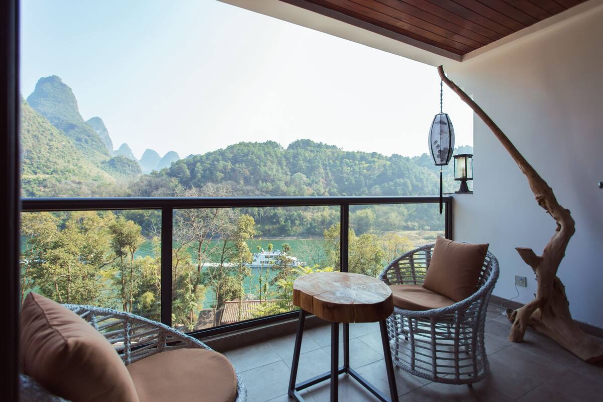 A balcony with wicker furniture, a view of a lake, and a mountain backdrop.