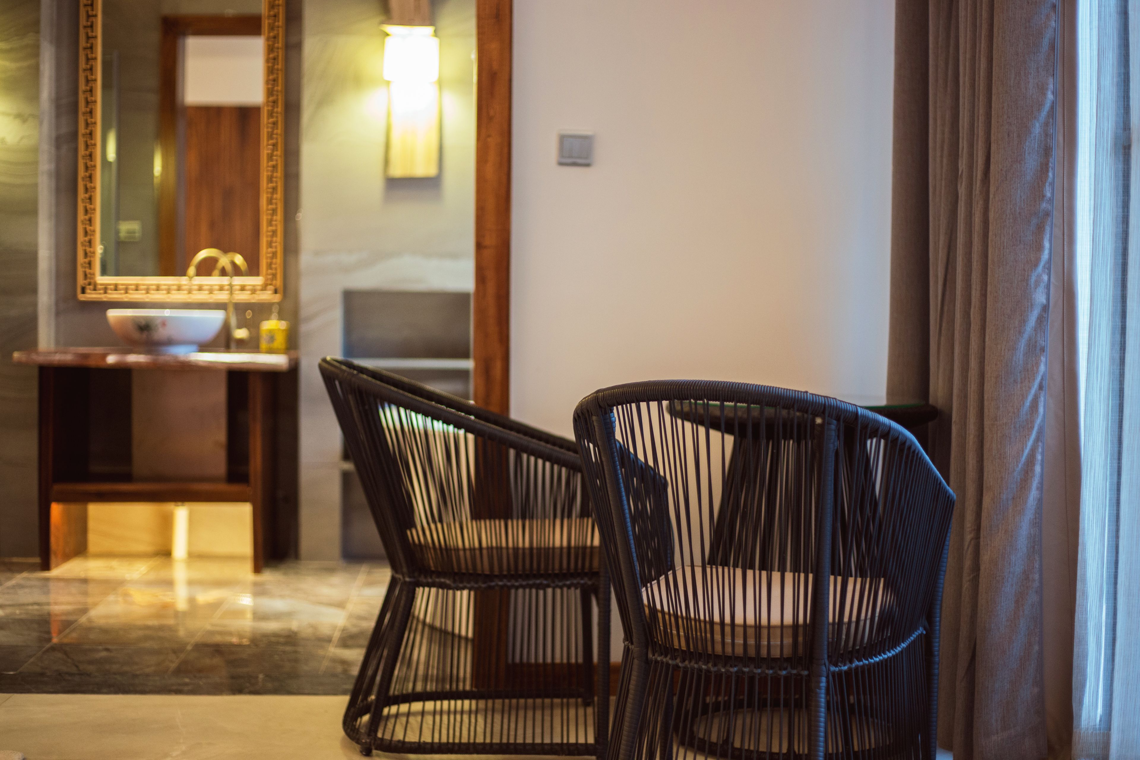 A hotel room with a large mirror, a sink, and two wicker chairs.