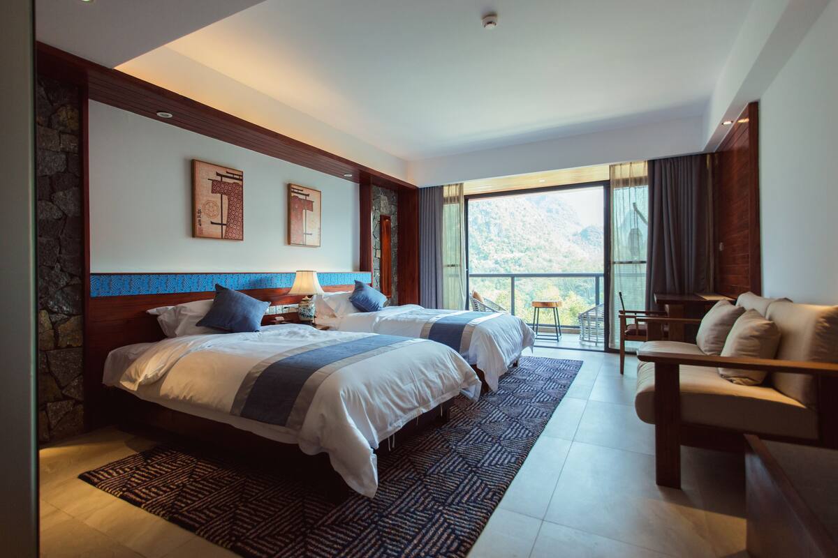 A hotel room with two beds, a balcony with a chair, and a large window.