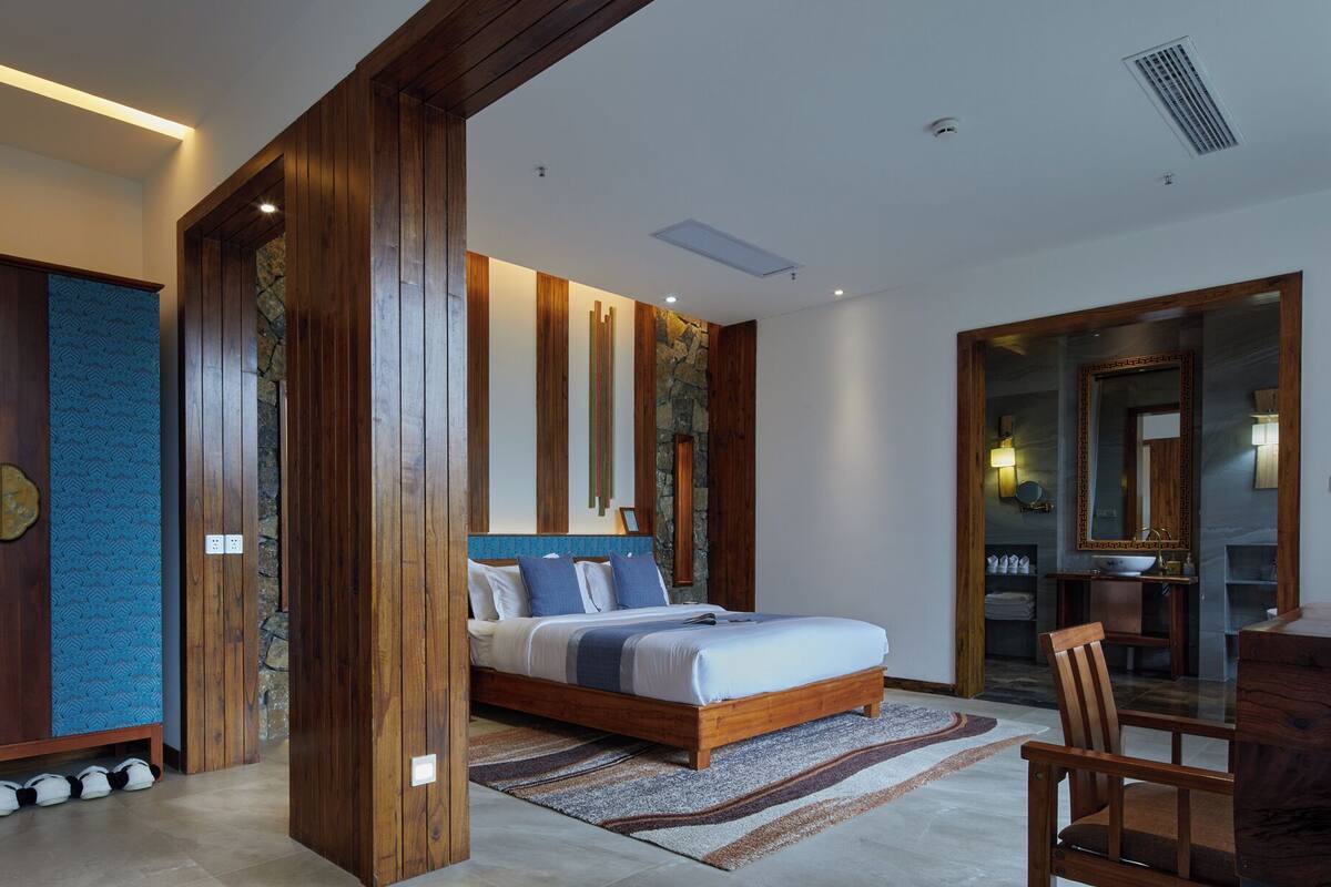 A modern bedroom with a wooden bed, a large mirror, and a stone accent wall.