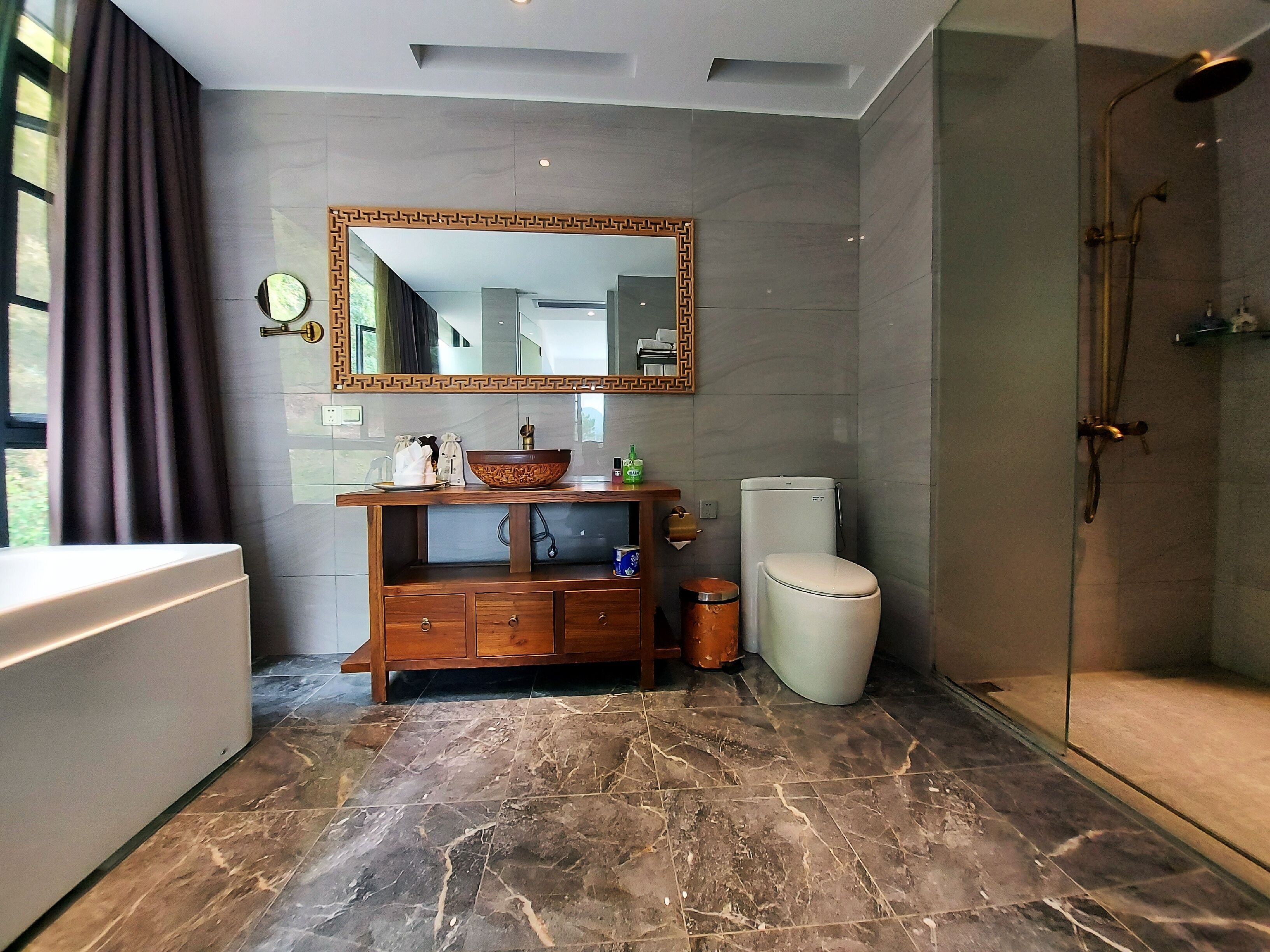 Un baño moderno con piso de mármol, tocador de madera, un espejo grande, inodoro y zona de ducha.