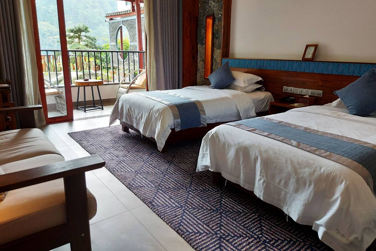A hotel room with two beds, a balcony with a view of a traditional building, and a wooden headboard.