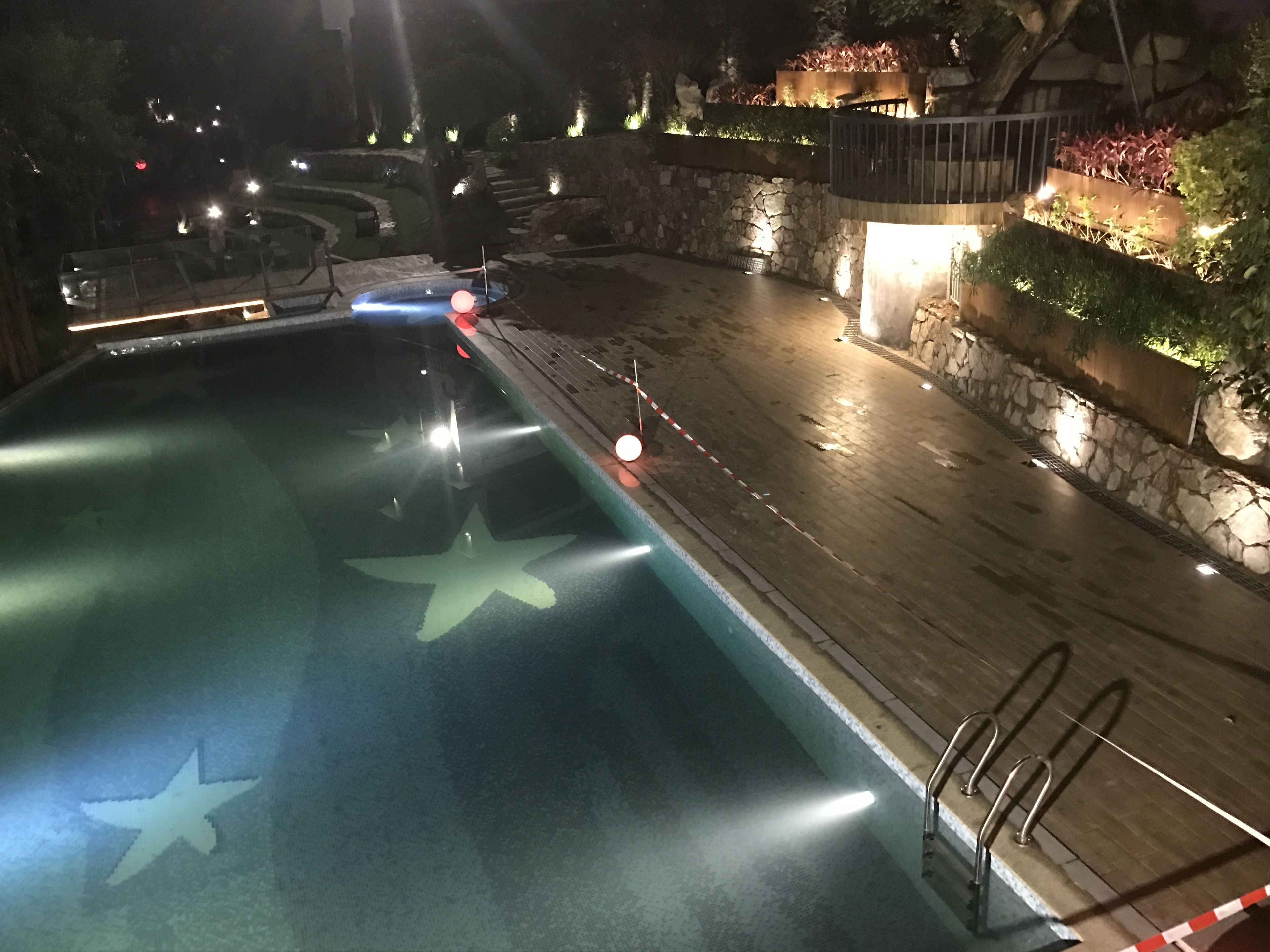 A swimming pool with a starfish design, surrounded by stone walls and illuminated by lights.