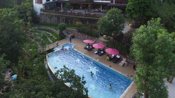 A hotel with a swimming pool surrounded by lush greenery and traditional architecture.