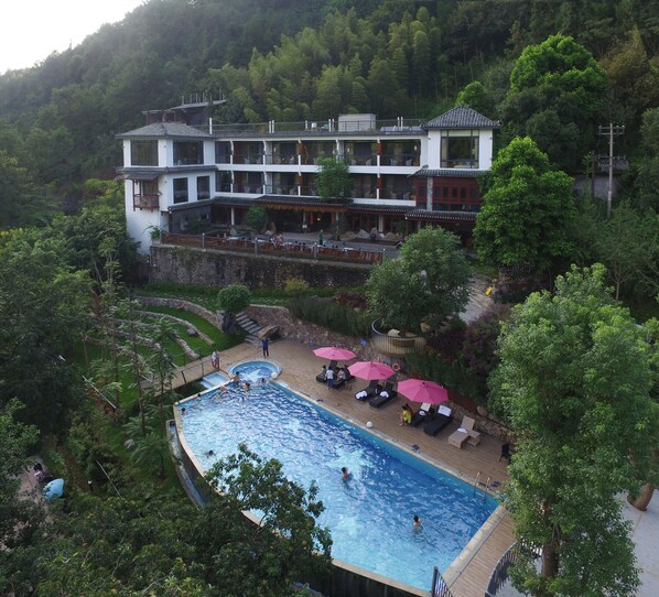 A hotel with a swimming pool surrounded by lush greenery and traditional architecture.