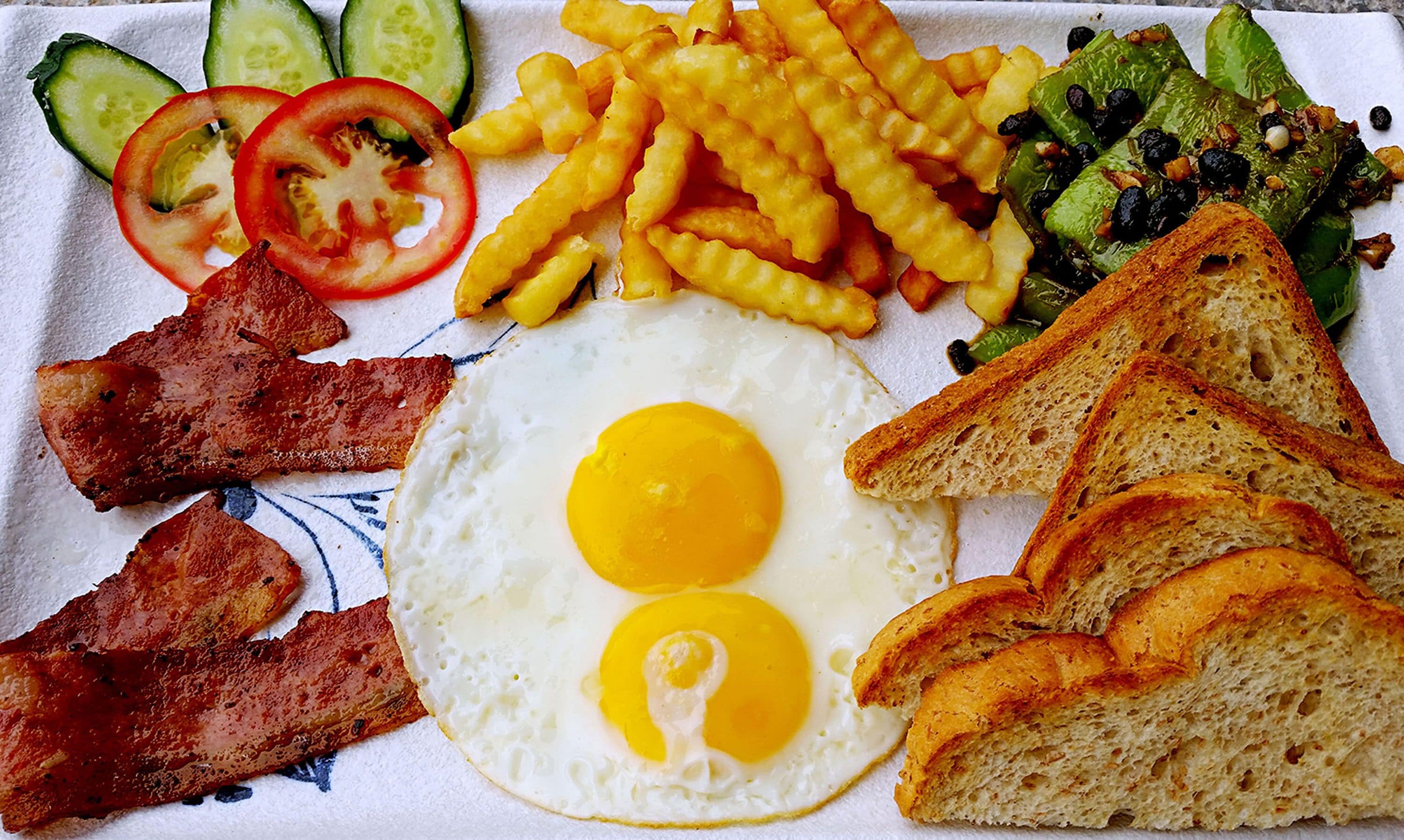 Een ontbijtbord met eieren, spek, toast, friet en groenten.